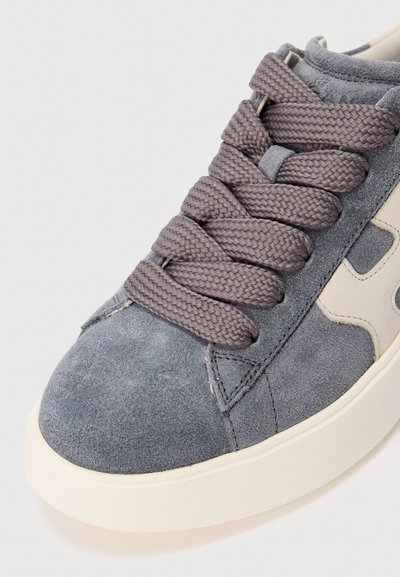 Grijze suede sneaker met dikke donkergrijze gevlochten veters en een lichtbeige zool, met een close-up van de voor- en zijkantdetails.