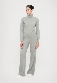 Grauer Strickrollkragenpullover mit geripptem Muster, kombiniert mit passenden weit geschnittenen Hosen, beide aus weichem, leichtem Material.