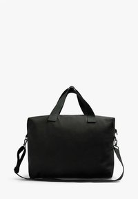 Bolsa de viaje de lona negra con dos asas en la parte superior y una correa de hombro ajustable. Presenta una forma rectangular y un cierre de cremallera en un lado.