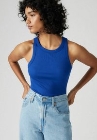 Top blu ribbed con scollo rotondo, abbinato a jeans azzurri a vita alta con chiusura a bottone e classico design a cinque tasche.