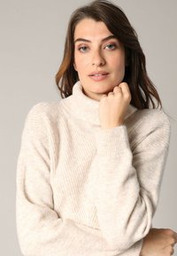 Pull à col roulé en crème avec texture côtelée, tissu doux, manches longues et léger éclat. Présente une coupe décontractée et un col haut.