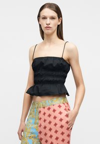 Γυναίκα που φοράει μαύρο ριγέ crop top με λεπτές τιράντες και ψηλόμεσο παντελόνι με ροζ και μπλε μπαρόκ σχέδια, χέρι στην τσέπη.