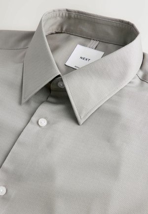 Grå skjorte med knaplukning lavet af struktureret stof. Har en spids krave, et mærke med "NEXT" og to hvide knapper foran.