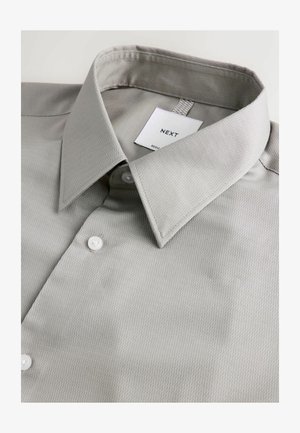 Pelēka pogām ar augstu apkakli izgatavota no faktūras auduma. Iespējas ietver vērstu apkakli, birku ar "NEXT" un divas baltas pogas priekšā.