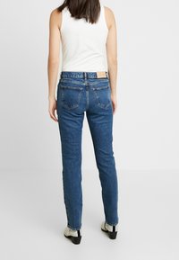 Jeans de tiro alto en azul oscuro, con corte recto. Con cinco bolsillos y una etiqueta de cuero en la cintura trasera. Tejido texturizado.