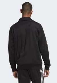 Giacca nera a maniche lunghe con colletto e polsini elasticizzati, caratterizzata da una superficie texturizzata e dettagli verdi sulle spalle.