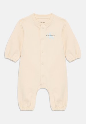 Tutina beige in cotone per neonati con maniche lunghe a sbuffo, bottoni a pressione lungo il davanti e un logo colorato di Calvin Klein sul petto.
