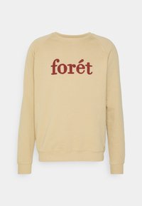 Sudadera de cuello redondo beige con mangas largas y el texto "forét" en rojo, texturizado, centrado en el pecho.