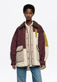 Chaqueta acolchada en burdeos, beige y oliva con diseño de acolchado texturizado, cuello con ribete de piel sintética y dos bolsillos frontales con tapetas de botón.