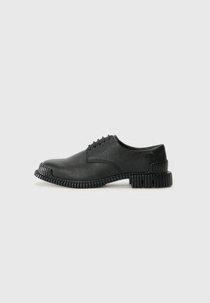Scarpe nere in pelle con finitura texturizzata, caratterizzate da una punta tonda e una suola in gomma con righe distintive. Quattro occhielli per i lacci.