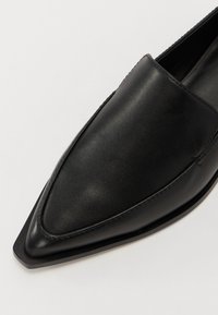 Mocasín negro de cuero con punta afilada, textura suave, costuras mínimas y suela plana. Sin herrajes ni acentos visibles.