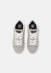 Gray suede sneakers with white laces and rubber soles. Features a black insole with a logo and a yellow label on the side.