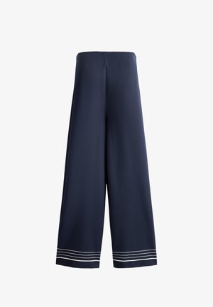 Tmavomodré nohavice s širokými nohavicami a vysokým pásom, so štyrmi tenkými bielymi vodorovnými pruhmi blízko spodného okraja na oboch nohaviciach.