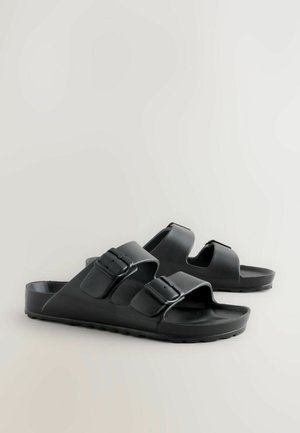Schwarze Rutsch-Sandalen aus strapazierfähigem Kunststoff, ausgestattet mit zwei verstellbaren Riemen mit Schnallen, einer geformten Fußbett und einer strukturierten Außensohle.