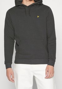 Sudadera con capucha de color gris oscuro, con un bolsillo frontal, puños acanalados y un pequeño logo amarillo en el pecho. Fabricada con tela suave.