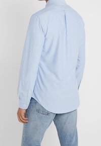 Ljusblå långärmad skjorta i bomull, med en bakveck, rundad nederkant och knappade ärmavslut. Bärs med denimjeans.