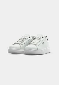 Adidași din piele albă cu o textură netedă, vârf rotund, talpă plată albă și accent negru la călcâi. Au șireturi plate și detalii cu logo.