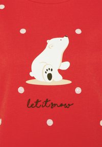 Camisa roja con una ilustración de un oso polar y el texto "let it snow" en cursiva negra. Con lunares blancos.