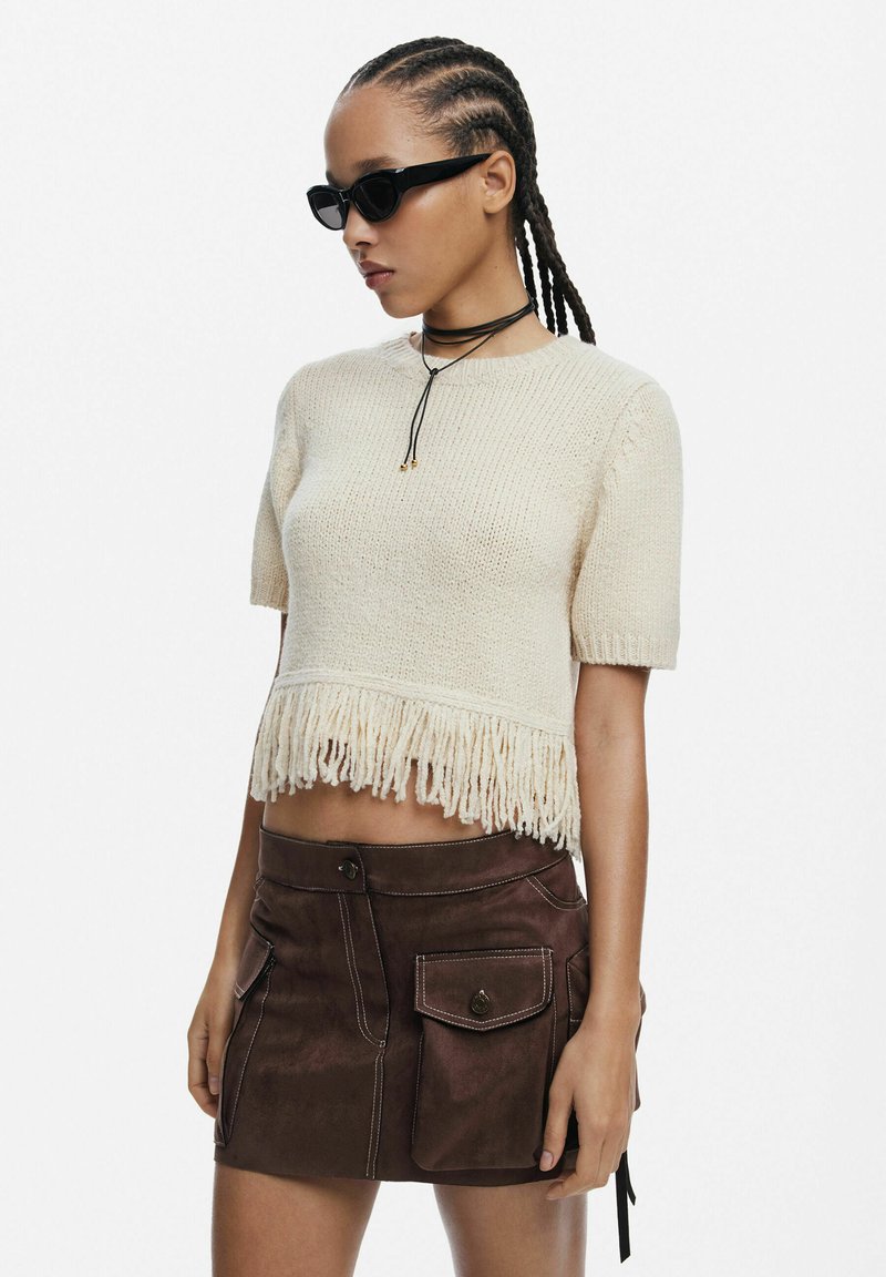 Kreemist kudumist crop-top, millel on frantsiidi äär, koos pruunist sametist seelikuga, millel on jootspockets ja kontrastsed õmblused. Kanda selget päikeseprille.