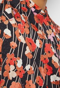 Chemise noire avec un motif floral rouge, orange, blanc et rose et des tiges crème fines et verticales, boutonnée au col.