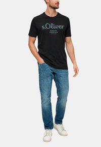 Černé bavlněné tričko s logem "s.Oliver" a grafickým textem, doplněné modrými džíny a bílými teniskami. Ležérní střih a klasický design.