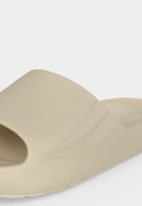 Μπεζ σανδάλι με ένα λουράκι, ανάγλυφη ανατομική σόλα και φαρδιά λωρίδα με διακριτικές ανάγλυφες γραμμές για υφή και στυλ.