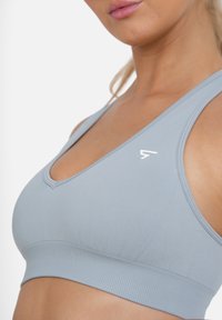 Light blue sports bra made of smooth, stretchy fabric. Features a V-neck design and a ribbed underband. Includes a small white logo accent.
