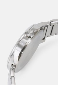 Montre-bracelet en acier inoxydable avec un boîtier rond, des tons argentés, une couronne de marque et un bracelet à maillons au design poli.