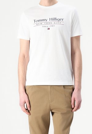 Biała bawełniana koszulka z nadrukowanym granatowym logo "Tommy Hilfiger New York City Since 1985" na wysokości klatki piersiowej. Krótkie rękawy i okrągły dekolt.