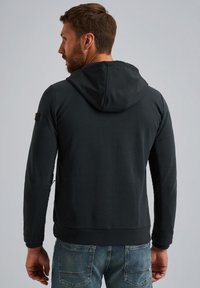 Zwarte hoodie met een gestructureerde afwerking, verstelbare capuchon en zijk verwijzingen. Gekozen in combinatie met blauwe spijkerbroeken, wat een casual stijl laat zien.