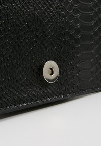 Borsa nera in finta pelle di serpente con texture e chiusura a scatto argentata lucida. Presenta una superficie liscia e un motivo distintivo a scaglie di serpente.