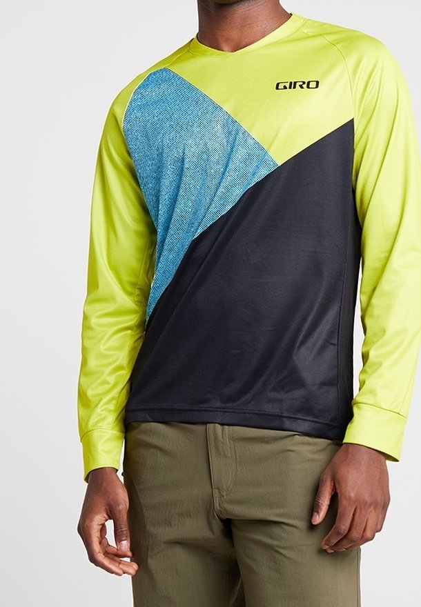Homme portant un maillot de cyclisme à manches longues avec des blocs de couleurs jaune, bleu et noir et un pantalon vert olive.