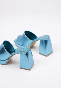 Mules en métal bleu avec un large talon carré et une bride large à l'arrière ouvert. Texture lisse et design à bout carré, avec un logo de marque discret sur la semelle intérieure.