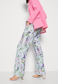 Lichtblauwe stoffen broek met bloemenpatroon in verschillende kleuren, met een relaxed fit, gecombineerd met lichtroze hoge sandalen.