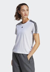 Witte sportt-shirt met zwarte strepen op de schouders, gemaakt van gladde stof. Bevat een Adidas-logo op de borst. Gecombineerd met grijze broek.