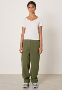 Bijela pamučna majica s V-izrezom u paru s opuštenim hlačama maslinasto zelene boje, teksturiranim i sivim tenisicama. Jednostavan dizajn, mekani materijal, neutralne boje.