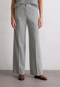 Pantaloni larghi grigi realizzati in un tessuto morbido, con chiusura a un solo bottone e tasche frontali, abbinati a scarpe marroni.