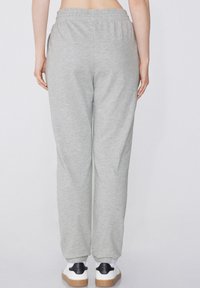 Pantalones de chándal grises con cinturilla elástica y bolsillos laterales, con puños acanalados en los tobillos. La tela tiene una textura suave y lisa.