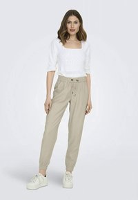 Top tricotat alb, ușor, cu decolteu pătrat, asociat cu pantaloni jogger bej cu talie elastică și adidași albi. Design simplu și casual.