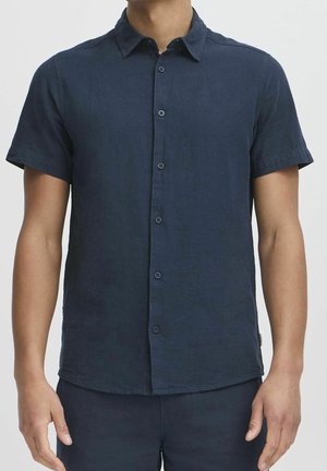 Mand iført en kortærmet, mørkeblå button-up skjorte med krave, vist fra nakke til hofter mod en ensfarvet baggrund.