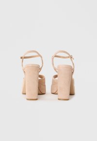 Beige mokkasandaler med hæl, ankelrem og enkelt rem over fronten. Glat tekstur med mat finish.