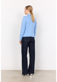 Sacou bleu deschis cu un design ajustat, asociat cu pantaloni evazați din denim închis. Întreaga ținută are mâneci lungi și detalii discrete de cusătură.