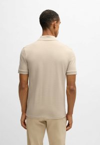 Beige kortärmad polo med en platt krage och upprullade ärmslut, som visar en slät textur och en figurnära design.