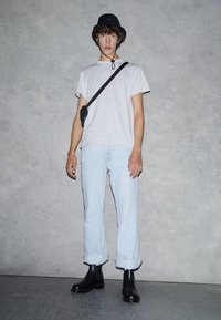 White t-shirt, light blue rolled-up jeans, black ankle boots, and a black bucket hat. Model poses against a grey background.