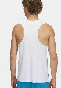 Top deportivo blanco sin mangas con diseño de espalda nadadora y textura perforada en la parte posterior, combinado con pantalones cortos azules.