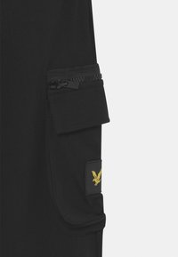 Czarne bawełniane spodnie cargo z boczną kieszenią na zamek i naszywką z złotym logo orła. Gładka faktura, przylegający krój.