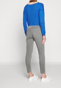 Niebieski top z długim rękawem o swobodnym kroju, zestawiony z szarymi obcisłymi dżinsami. Modelka ma na sobie białe trampki ze złotym zdobieniem na pięcie.