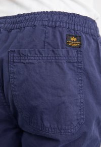 Shorts bleu marine à coupe décontractée avec une taille élastique, présentant une poche plaquée à l'arrière et une étiquette de logo jaune.