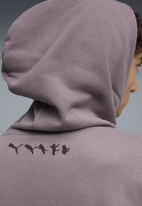 Sudadera con capucha en lavanda clara, con una textura suave y un gráfico de color púrpura oscuro de cinco animales saltando en la parte posterior.