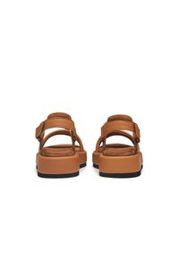 Tan sandals with a wide strap, open back, and a padded insole. Textured suede and smooth synthetic materials; flat black sole.